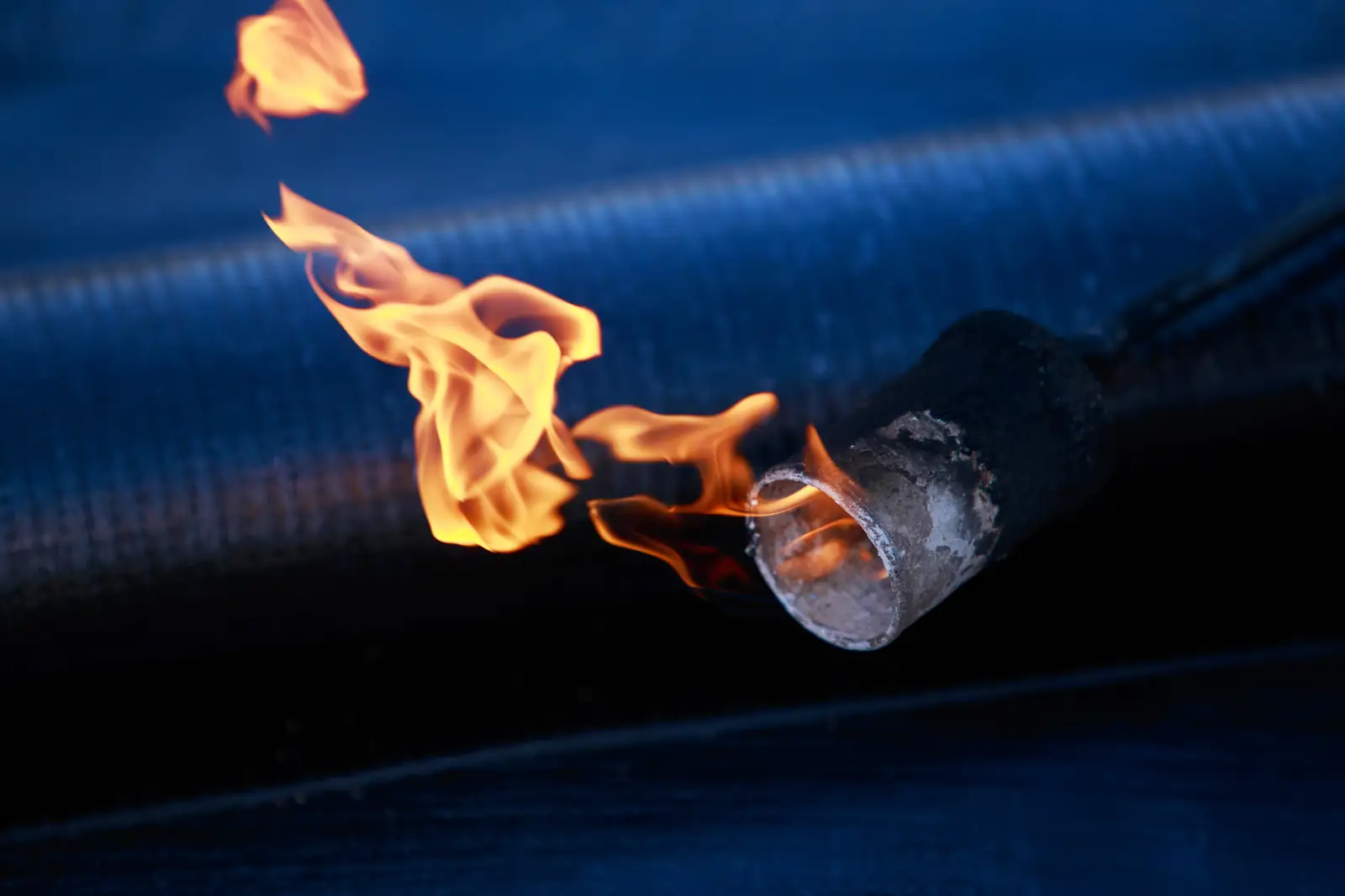 Close-up of a roofing torch flame heating a felt membrane
