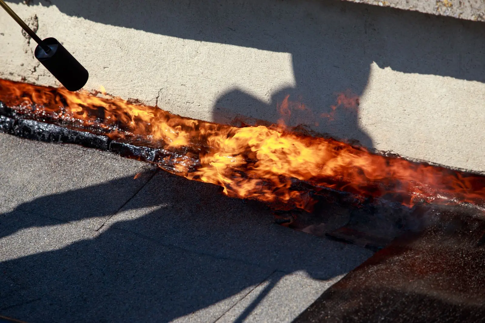 Roofing torch flame heat-bonding felt along the edge of a flat roof