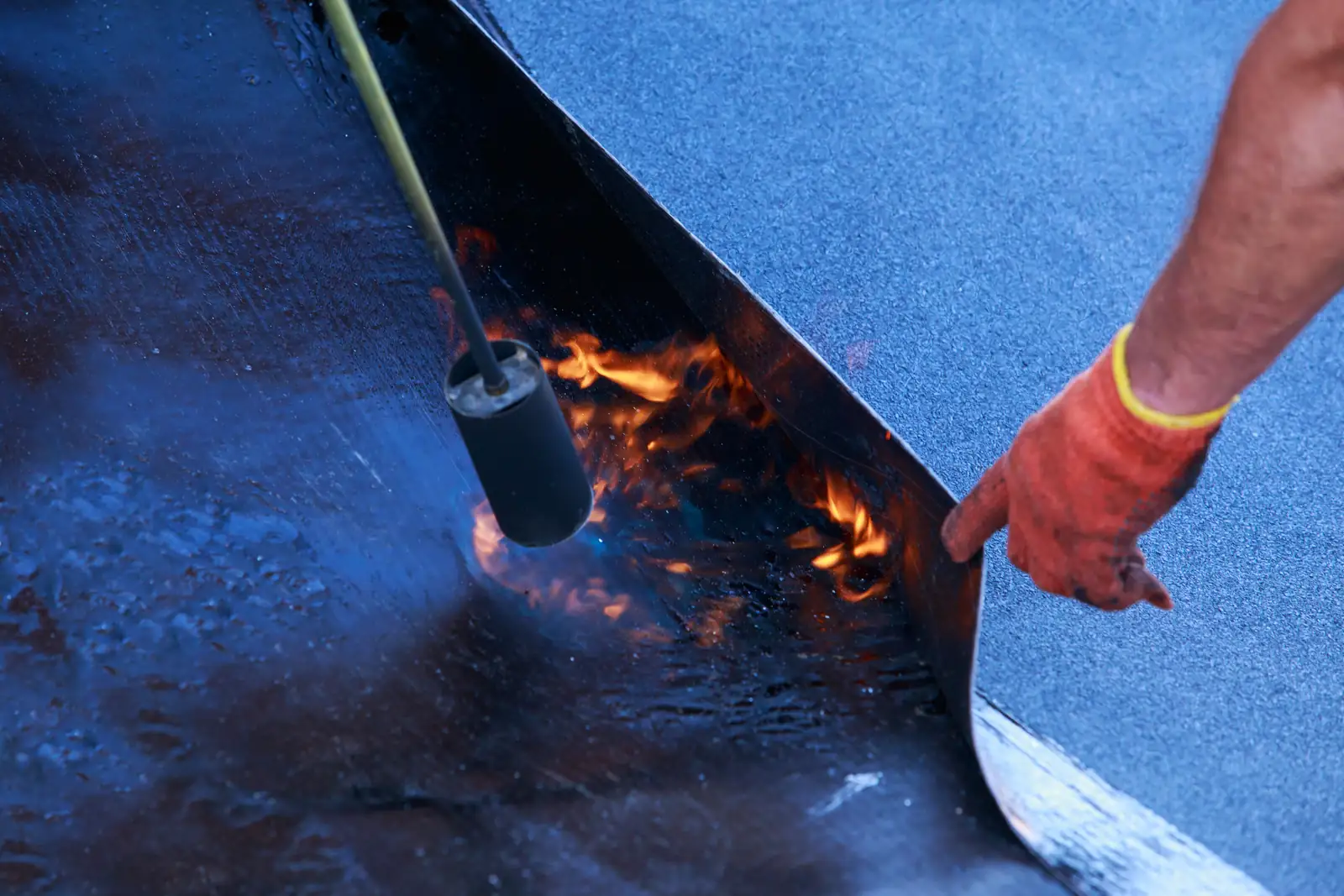 Roofer heat-bonding the underside of a roofing membrane with a torch